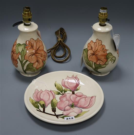A pair of Moorcroft Hibiscus pattern table lamps and a Magnolia pattern plate, H 28cm (lamp) Dia 26cm (dish)